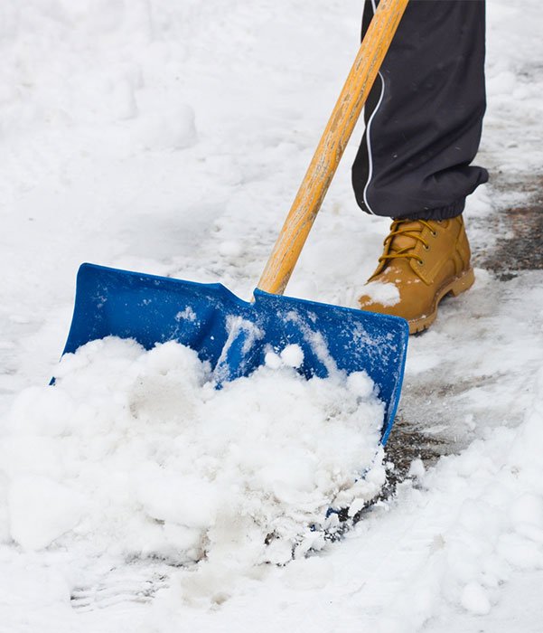 Individual using a blue shovel to clear snow from a driveway on a winter day.