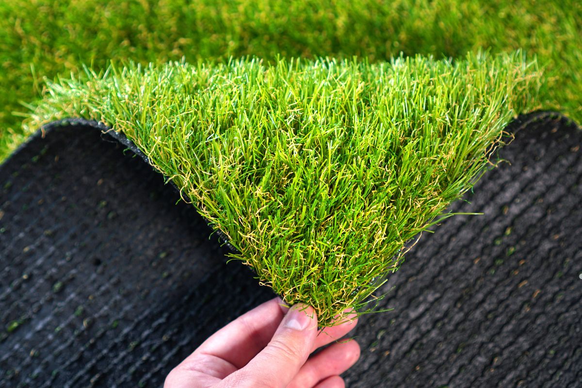A person showcasing a piece of artificial grass, representing a lawn care service's offerings for a lush, maintenance-free yard.